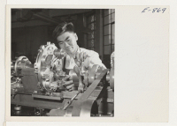 [recto] Kenneth Sugioka, young Nisei, at work on a precision lathe in the defense plant of the Hathaway Instrument Company in ...