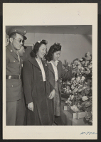 [recto] Two Japanese-American soldiers, home on furlough and their girl friends viewing the flower booth at the Arts and Crafts Festival. These artificial flowers were made at the center by students who attended night school classes. ;  Photographer: Coffey, Pa
