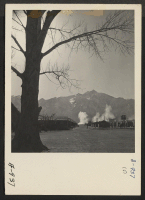 [recto] A view of the Manzanar Relocation Center, with Mount Whitney, highest mountain in the continental United States, in the background. The smoke in the distance is caused from burning trash. ;  Photographer: Stewart, Francis ;  Manzanar, California.