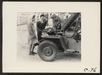 [recto] Arcadia, Calif.--Two young evacuees of Japanese ancestry watch an army mechanic repair a Jeep at Santa Anita assembly center. ;  Photographer: Albers, Clem ;  Arcadia, California.
