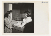 [recto] Mrs. Mari Yashida looks at her baby through the plate glass window of the nursery, as nurse's aide Nobuko Hirashima returns it to its crib after feeding. ;  Photographer: Iwasaki, Hikaru ;  Heart Mountain, Wyoming.