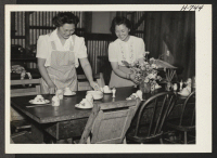[recto] Mrs. Mary Terada (left) and Miss Yuri Kawakami, both of Heart Mountain, set the table at the Civic Unity Hostel in San Jose. Mrs. Terada, with her husband and two young daughters, arrived on June 7. They are stopping at the hostel while looking for a hous