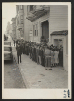 [recto] Lining up before Japanese American Citizens League auditorium at 2031 Bush Street to register for evacuation. Evacuees of Japanese ancestry will be housed in War Relocation Authority centers for the duration. ;  Photographer: Lange, Dorothea ;  San Fr
