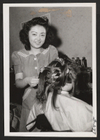 [recto] Miss Tokiko Ann Tanaka giving a permanent wave in the Economy Beauty Shop, which she owns and operates on upper ...
