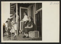 [recto] Closing of the Jerome Center, Denson, Arkansas. An Issei couple sit on their porch and watch their belongings being loaded on trucks for movement to another center. ;  Photographer: Iwasaki, Hikaru ;  Denson, Arkansas.