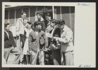 [recto] A group of Heart Mountain high school students gathers around the entrance to the principal's office with Ralph Forsythe, assistant principal. ;  Photographer: Hosokawa, Bill ;  Heart Mountain, Wyoming.