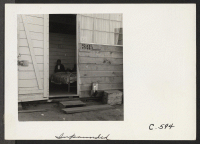[recto] A close-up of an entrance of a family apartment (converted horse stall). Note that the windows in this unit have been enlarged. Five people occupy two small rooms, the inner one of which is without outside door or window. ;  Photographer: Lange, Dorothe
