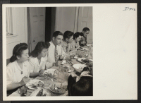 [recto] At supper in the dining room of the Greater New York Relocation Hostel is a typical group of temporary residents, ...