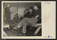 [recto] Lt. Eugene Bogard explaining the purpose of registration to Japanese and Japanese-Americans. Similar meetings were held at all centers for the purpose of registering all evacuees between the ages of 18 and 38. ;  Photographer: Stewart, Francis ;  Manz