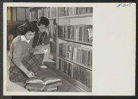 [recto] Scene in the Heart Mountain High School library, as Miss Mickey Yabe helps a fellow student with some research work in ancient history. ;  Photographer: Iwasaki, Hikaru ;  Heart Mountain, Wyoming.