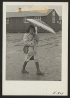 [recto] The Arkansas rainy season, and this young resident of the Jerome Center dons rubber boots and carries a parasol. The (buckshot) mud makes the trip to and from school a little difficult. ;  Photographer: Parker, Tom ;  Denson, Arkansas.