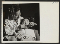 [recto] Dr. H. Nakahara, head of the dental clinic at the Heart Mountain Hospital, is shown examining teeth of one of the center's residents. ;  Photographer: Iwasaki, Hikaru ;  Heart Mountain, Wyoming.