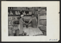 [recto] The interior of the storeroom at Mess Hall 7. Chief cook Hamazaki receives supplies from storekeeper Jimmy Saito. ;  Photographer: Parker, Tom ;  Denson, Arkansas.