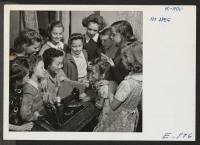 [recto] A group of eager students gather around their instructor, Tetsu Sugi, in a children's sewing class at Christopher House in ...