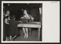 [recto] Scene in the induction center at Tule Lake as new arrivals from Topaz pass through the various departments before being directed to their new quarters. Here a mother and her three children are shown registering. ;  Photographer: Mace, Charles E. ; , .