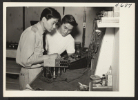 [recto] Satoru Akutagawa (left) and Jiro Oishi at work in their new radio service shop, 1856 E. Colorado Boulevard, Pasadena. The ...