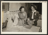 [recto] These attractive young evacuees show the garments made by the pattern drafting class in Block 1308. (L to R) Mary Arima, Mrs. Alice Tsukuno. ;  Photographer: Stewart, Francis ;  Newell, California.