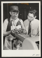 [recto] Harry Bostram, Chief Machinist in charge of tool and design [illegible], checks the operation of a model machine, in the ...