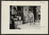 [recto] One worker of the six man beet topping crew is sent to the farmhouse to [prepare] dinner while the rest of the crew work till sundown. Here George Adachi [illegible] the rice steaming on the kitchen stove. ;  Photographer: Parker, Tom ; , .