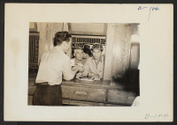 [recto] Manzanar, Calif.--Evacuee of Japanese ancestry receiving mail at Manzanar Post Office--a branch of the Los Angeles Post Office, more than 250 miles away. A two-cent stamp will send a letter by first-class mail from Manzanar to Los Angeles. ;  Photograph