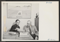 [recto] Harry Makino, manager of the Tule Lake poultry farm, is shown talking to Clarence Zimmer, in charge of agriculture and industry at this project, in the office of the poultry farm. ;  Photographer: Stewart, Francis ;  Newell, California.