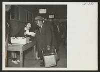 [recto] An elderly Issei gentleman arriving on trip 14 from Tule is here shown being directed to his new quarters by one of the volunteer workers in the induction center. ;  Photographer: Mace, Charles E. ;  Topaz, Utah.