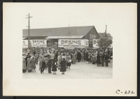 [recto] Awaiting evacuation bus, while personal effects are packed aboard moving vans. Evacuees of Japanese ancestry will be housed in War Relocation Authority centers for the duration. ;  Photographer: Lange, Dorothea ;  Centerville, California.