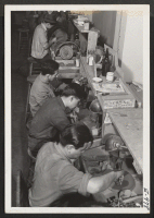 [recto] In a Manhattan lapidary plant, a group of relocated Nisei representing nearly all the relocation centers, are employed at the highly skilled trade of cutting and polishing semi-precious stones. ;  Photographer: Parker, Tom ;  New York, New York.