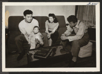 [recto] Takeshi Katayanagi, his wife Yaeko, his brother Kiyoshi, and his baby daughter, Kathryn relax in their Cleveland home. The family lived in Berkeley, California, and were sent to the Topaz Relocation Center. They came to Cleveland, where Takeshi works as a