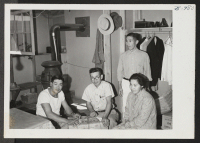 [recto] Mr. and Mrs. Ben Seikichi, center and right, with two friends. They are here shown packing their personal belongings preparatory to moving to another center. ;  Hunt, Idaho.
