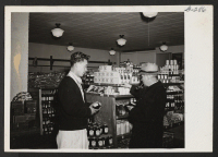 [recto] John Y. Nakagawa, formerly of Granada, who works in the produce department of the Media Cooperative store in Media, Pennsylvania, shows a customer the best buy. ;  Media, Pennsylvania.