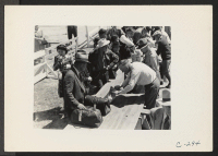 [recto] Turlock, Calif.--Heads of families of Japanese ancestry are gathered about the table where their hand-baggage is being inspected for contraband before being admitted into the Assembly Center. ;  Photographer: Lange, Dorothea ;  Turlock, California.