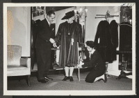 [recto] Miss Masako Matsunami is shown in this picture fixing the coat of a customer. The gentleman at the left, fixing ...
