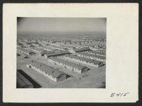 [recto] Overlooking the Amache Relocation Center, near Granada, Colorado. In the foreground is a typical barracks unit consisting of 12 six room apartment barracks buildings, a recreation hall, laundry and bathrooms, and the mess hall. ;  Photographer: Parker,