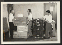 [recto] Personal effects arriving at the Oakland Hostel are being check by Saburo Sasaki, Gila River (left); Mr. Joseph S. Aoki, Topaz; and Mr. J. Yamashita, Topaz. The latter is director of the hostel. ;  Photographer: Mace, Charles E. ;  Oakland, California