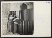 [recto] Three evacuees unloading prop charges from a box car at the Sioux depot. The prop charges are placed on a truck and transported to a storage place at the depot. ;  Photographer: Aoyama, Takashi ;  Sidney, Nebraska.