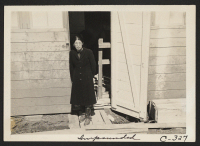 [recto] A Japanese woman, just evacuated, who arrived this morning is shown at the door of her living quarters. Each door enters into a family unit of two small rooms (remodeled horse-stalls). ;  Photographer: Lange, Dorothea ;  San Bruno, California.