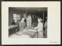 [recto] A young Nisei girl purchases Christmas wrappings in the cooperative notion store. ;  Photographer: Parker, Tom ;  Amache, Colorado.