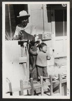 [recto] Evacuee boxes household effects with assistance of small daughter. ;  Newell, California.
