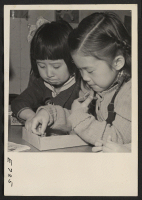 [recto] Two small girls, whose grandparents came to the United States from Japan, play with clay toys in the nursery school at the Heart Mountain Relocation Center. ;  Photographer: Parker, Tom ;  Heart Mountain, Wyoming.