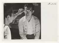 [recto] Optometrist Wright Kawakami, examines the eyes of Al Tanouye prior to fitting him with glasses. Dr. Wright Kawakami is a graduate of the University of California School of Optometry. ;  Photographer: Iwasaki, Hikaru ;  Heart Mountain, Wyoming.