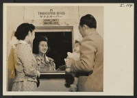 [recto] Mr. and Mrs. Thomas Oki and their small daughter, Dinne, checking out time with Dorothy Hiuga of the timekeepers division, ...