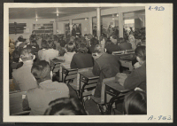 [recto] Lieutenant Eugene Bogard explaining registration purposes to a group of Japanese-Americans and Japanese who were evacuated from west coast defense areas. All persons between the ages of 18 and 38 were compelled to register. Seated is Sergeant Victor Tierm