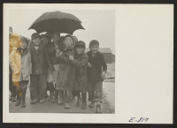 [recto] One umbrella wasn't enough for these lads of Japanese ancestry, who formerly lived in west coast areas. The rainy season, in Arkansas, makes the relocation center one vast quagmire. ;  Photographer: Parker, Tom ;  Denson, Arkansas.