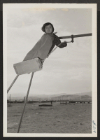 [recto] One of the young Heart Mountain school children is enjoying a swing on the center's play ground. ;  Photographer: Iwasaki, Hikaru ;  Heart Mountain, Wyoming.
