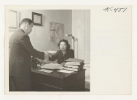 [recto] Lily Nakanishi, in San Francisco, hands an appointment slip for work to a recently returned evacuee. Lily operates an independent ...