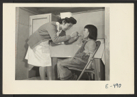[recto] The school nurse administers a throat swabbing to a young grade school student. One of the school barracks block is occupied by the school nursing staff, who maintains careful watch and administers, under the hospital doctor, ordinary medical treatment.