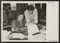 [recto] Albert Saijo, Echo editor, looks over copy being put on a mimeograph stencil by Shizu Yamaguchi, typist. ;  Photographer: Hosokawa, Bill ;  Heart Mountain, Wyoming.