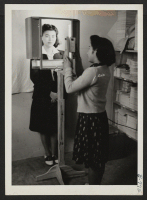 [recto] Dorothy Maruki having her identification picture taken with a new Identification Camera in Leave Office in order to leave the center. ;  Photographer: Okano, Tom K. ;  Dermott, Arkansas.