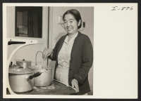 [recto] Mrs. Emon Ikuda, formerly of Heart Mountain, prepares a family meal on her own stove for the first time since evacuation. Mr. and Mrs. Emon Ikuda and their son Mitsuo were White River Valley's first returnees. ;  Photographer: Iwasaki, Hikaru ;  Kent,